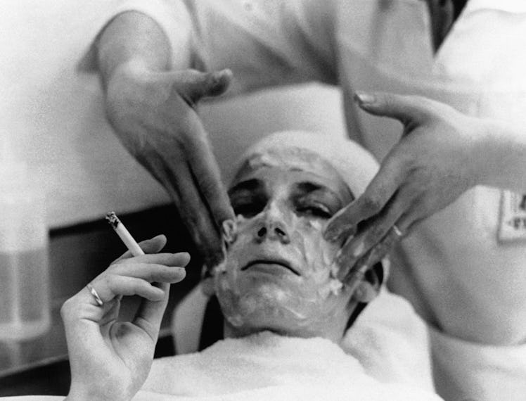 A woman smoking a cigarette why receiving a facial spa treatment by another woman