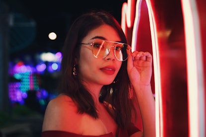 Young woman with glasses in red neon lights, ready to learn her zodiac sign's evil superpower.