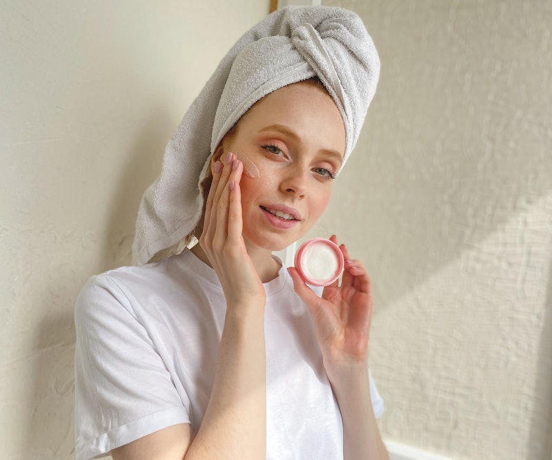 A woman with a towel on her head putting an overnight face mask on