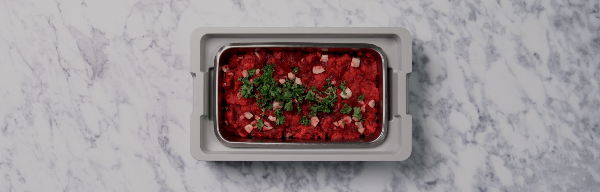 An aerial view of an open lunchbox on a marble countertop. A red, delicious looking slop is inside t...