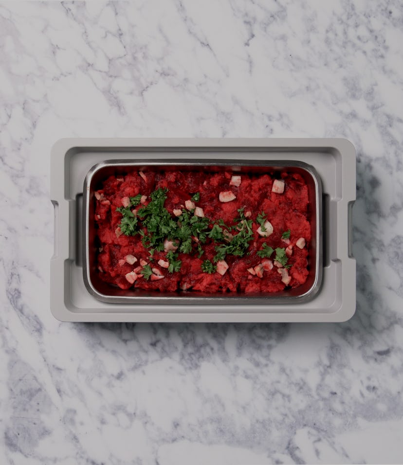 An aerial view of an open lunchbox on a marble countertop. A red, delicious looking slop is inside t...