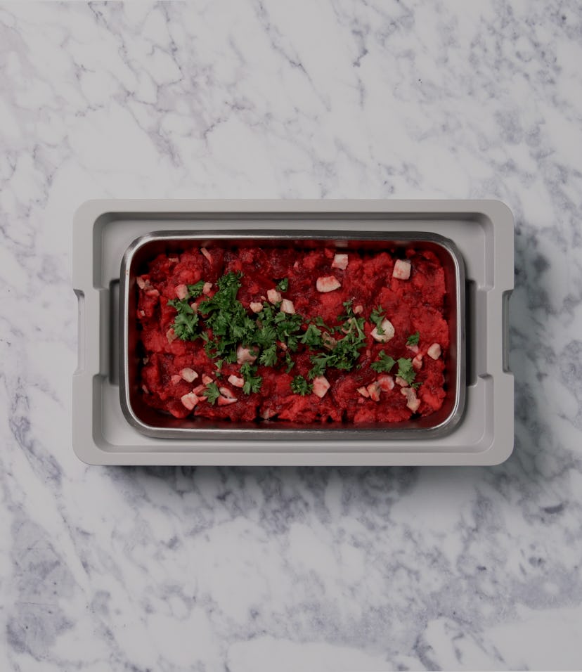 An aerial view of an open lunchbox on a marble countertop. A red, delicious looking slop is inside t...