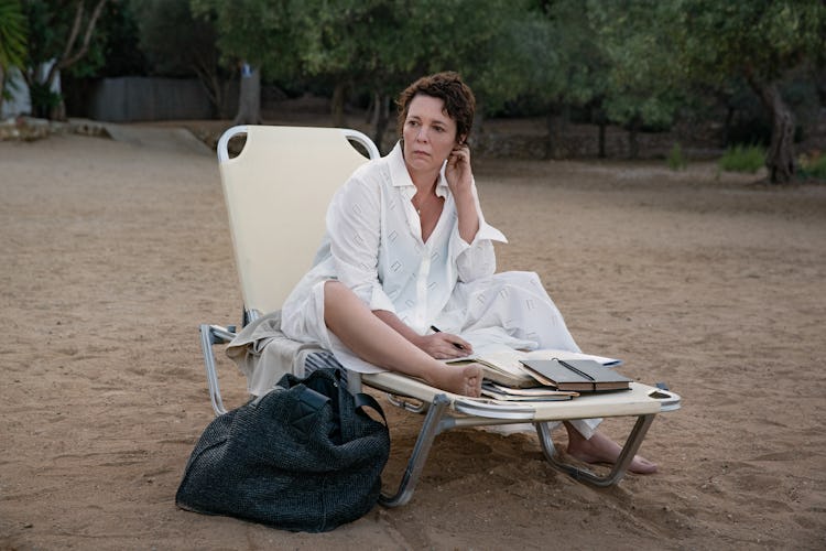 Olivia Colman as Leda, sitting on a beach chair with her work