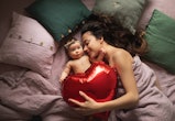 mom with newborn lying in bed, holding a red heart balloon for article about the best valentine's da...
