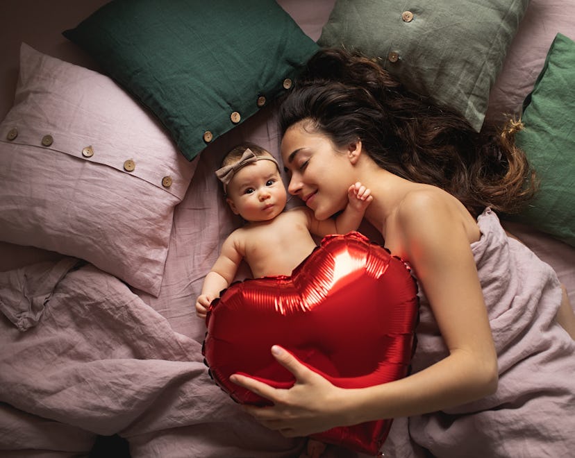 mom with newborn lying in bed, holding a red heart balloon for article about the best valentine's da...