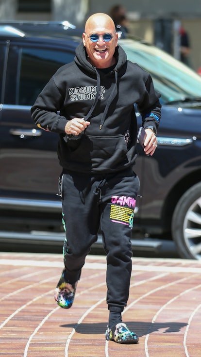 Howie Mandel running down a street and laughing in a black hoodie