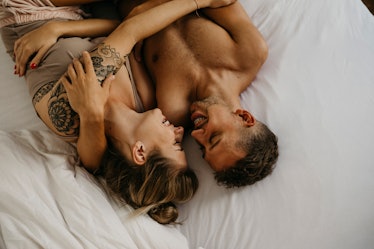 Man and woman laughing will holding each other in bed