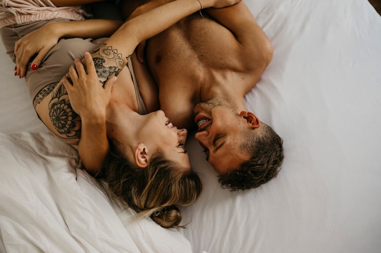 Man and woman laughing will holding each other in bed