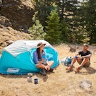 A couple camping with the help of a blue Coleman pop-up camping tent