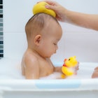 A baby in a tub getting a bath with a rubber duck bath toy.