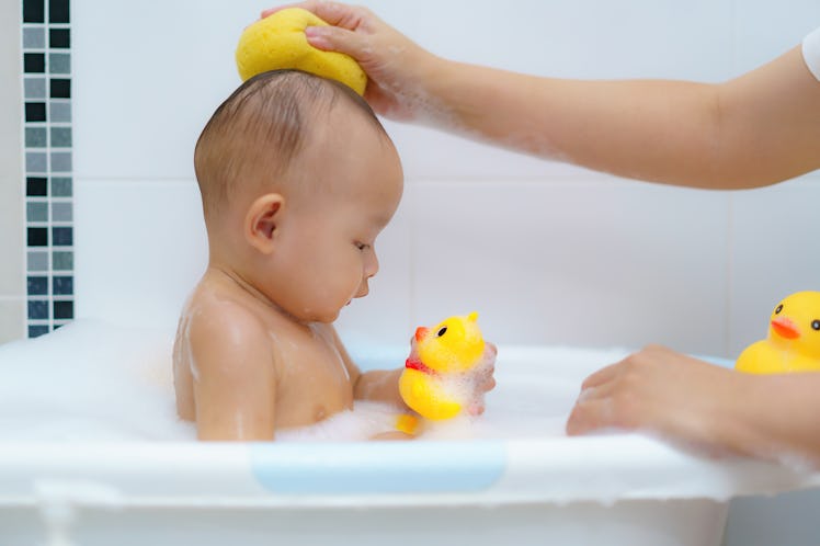 A baby in a tub getting a bath with a rubber duck bath toy.