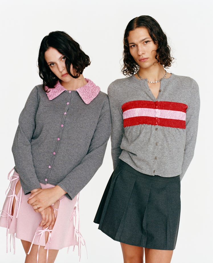 two models wearing miniskirts and grey cardigans with pink and red ribbon accents