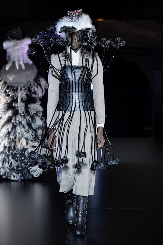 A model wearing a a grey checked suit-dress with a black corset and 3D floral elements by Noir Kei N...