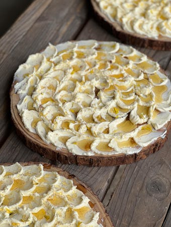 Butter on a round wooden board topped with honey, lemon zest, and flower petals