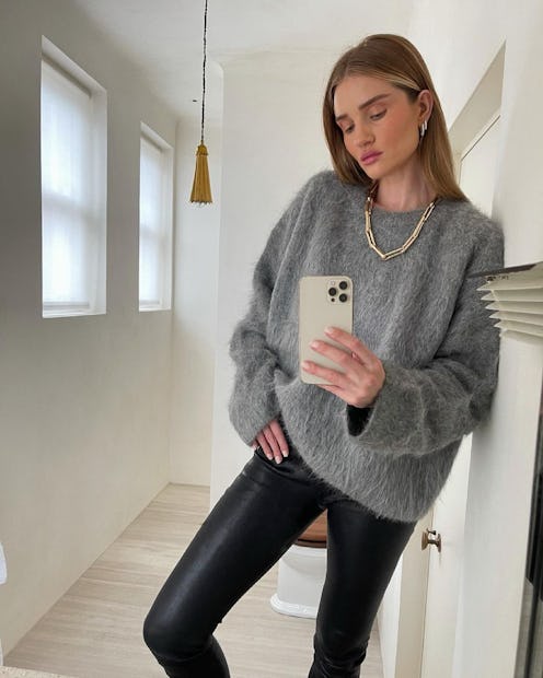 Rosie Huntington-Whiteley taking a mirror selfie in a grey sweater and black leggings