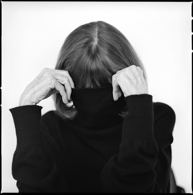 a black and white portrait of the writer Joan Didion hiding her face in a turtleneck sweater