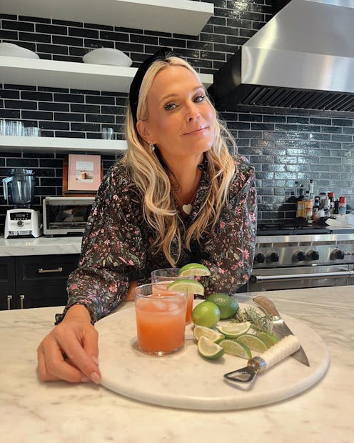 A blonde lady posing in her kitchen with two orange cocktail glasses and lime slices in front of her