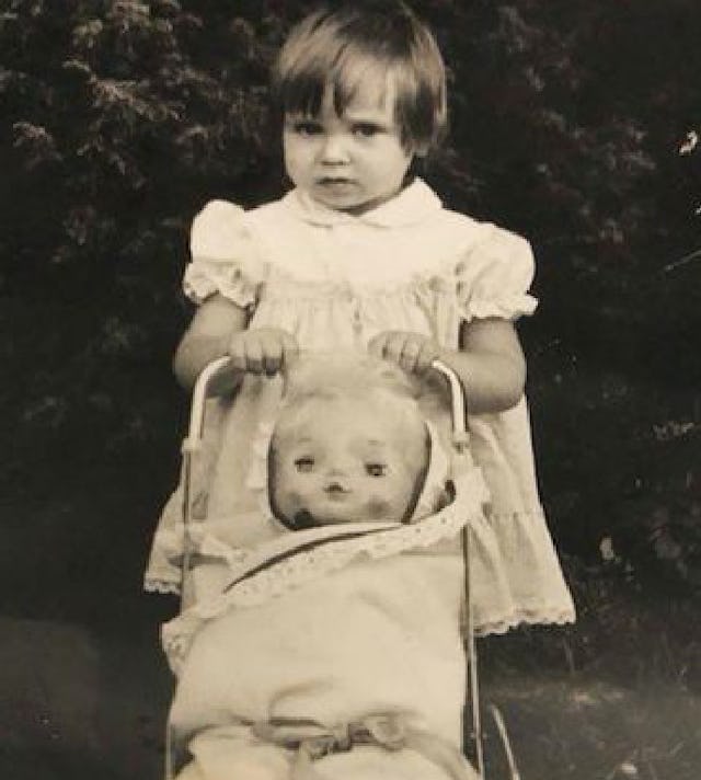 Janina as a toddler with a stroller and a doll inside of it