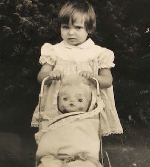 Janina as a toddler with a stroller and a doll inside of it