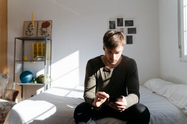 Man sitting on bed looking through phone