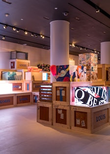 a view of a gallery space filled with wooden crates and artistic renderings of a trunk