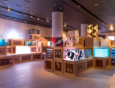 a view of a gallery space filled with wooden crates and artistic renderings of a trunk