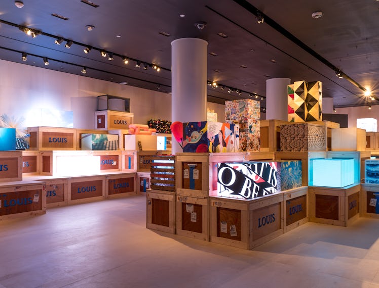 a view of a gallery space filled with wooden crates and artistic renderings of a trunk