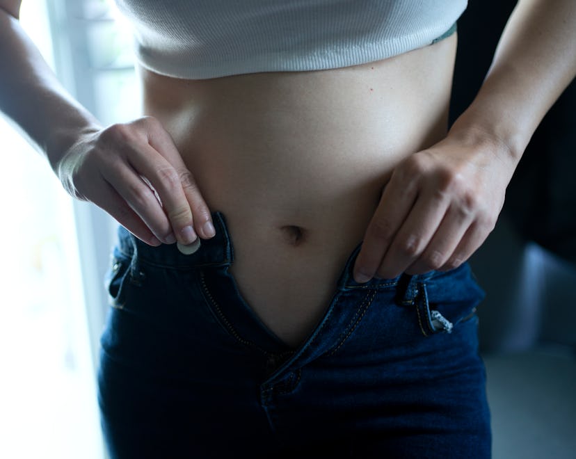 A woman in early pregnancy trying to button up her jeans.