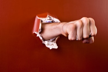 A man's fist punching a hole in a red wall.