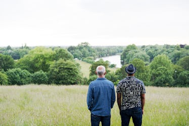 Two men in a field, looking into the distance: one in a short-sleeved shirt and fedora and the other...