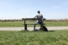 一名中年男子独自坐在公园长椅上，背对着镜头