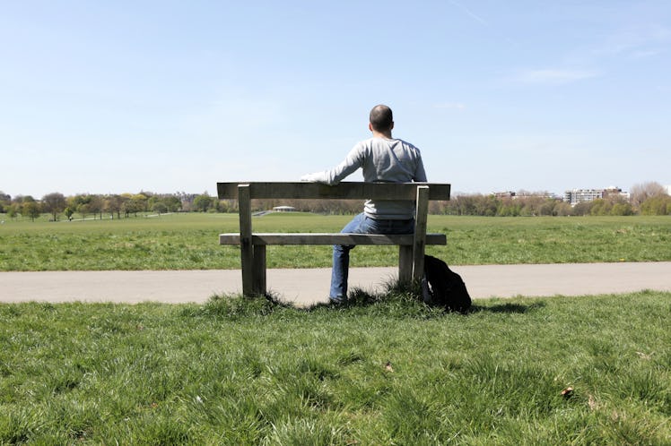Middle aged man sitting alone on a park bench facing away from camera