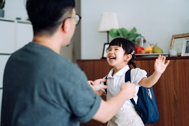 A dad helps his Kindergarten daughter get ready for school, adjusting her clothes at home.