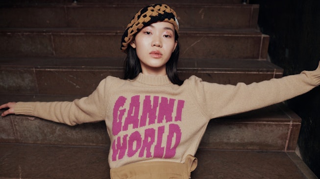 Ganni in a Ganni World shirt and a beret lying on stairs