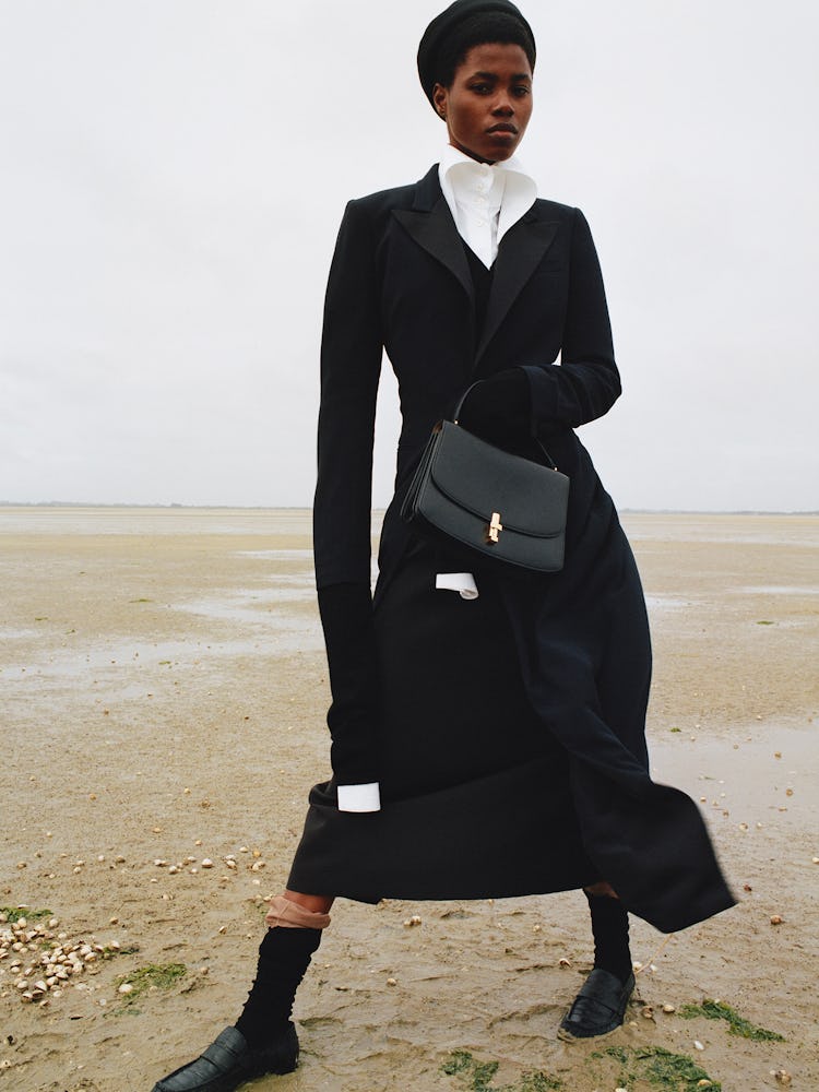 Victoria Fawole wears a black coat, bag, hat and shoes.