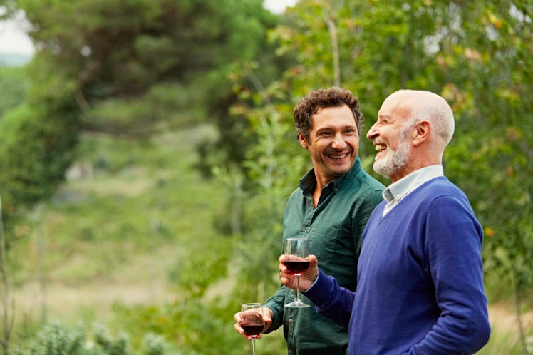 A father and son standing in a vinyard drinking glasses of wine and laughing