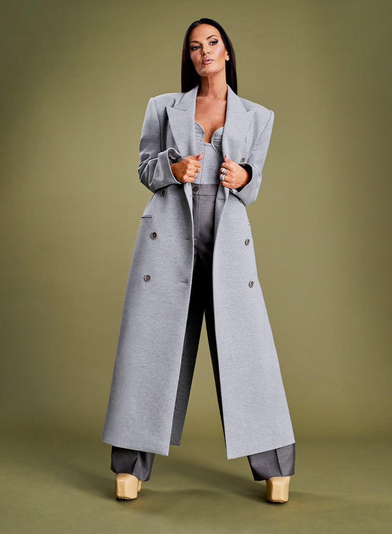 Lisa Barlow posing in a silver coat, grey pants and a grey corset top