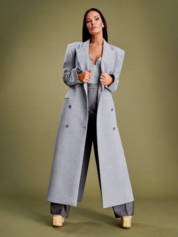 Lisa Barlow posing in a silver coat, grey pants and a grey corset top   