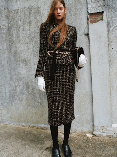 Nyiro wears a jacket, shirt, white gloves and leather bag.