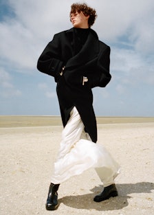 Greta Bultmann wears a Saint Laurent by Anthony Vaccarello coat, dress, and bracelets; Tod’s boots; ...