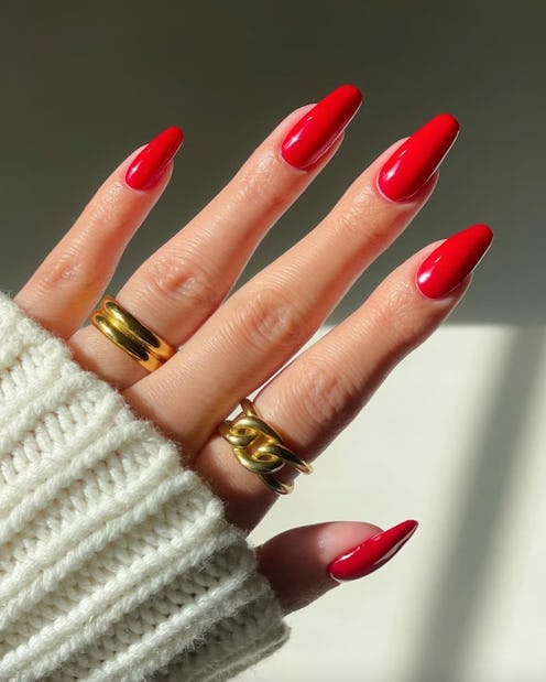 A female hand with long red nails and chunky golden rings