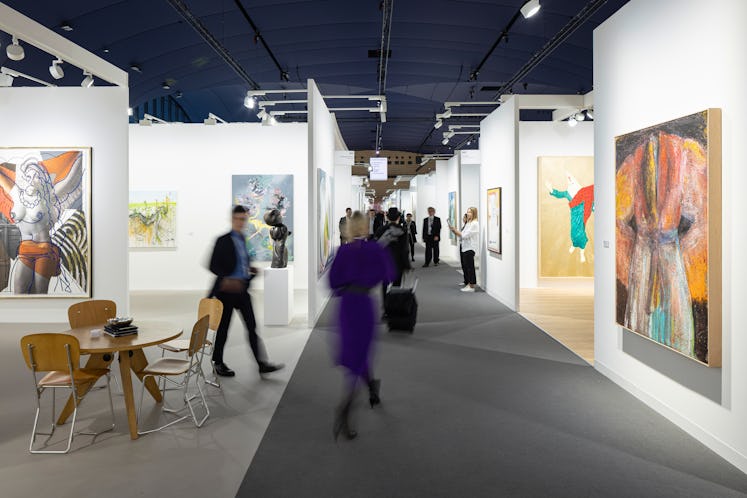 A view of an art fair, with booths filled with contemporary paintings 