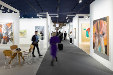 a view of an art fair, with booths filled with contemporary paintings and patrons walking through th...