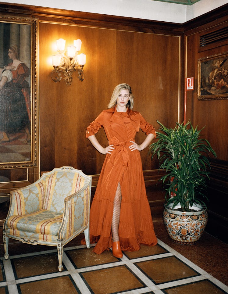 Lili Reinhart wearing an orange dress, shoes and fishnet stockings.