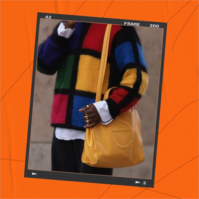 A person holding a Telfar IT orange bag while wearing a colorful square design sweater