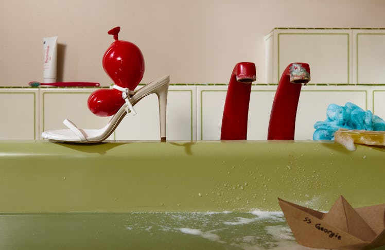 A white Loewe strappy sandal with their iconic red balloon adornment atop the sandal. The shoe is re...