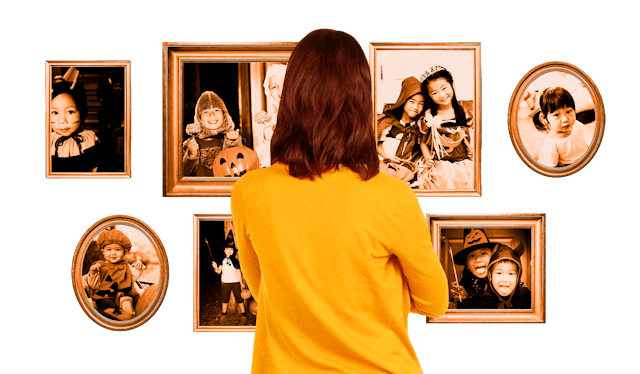 A mom in a yellow sweater looking at the photos of her kids' costumed for Halloween