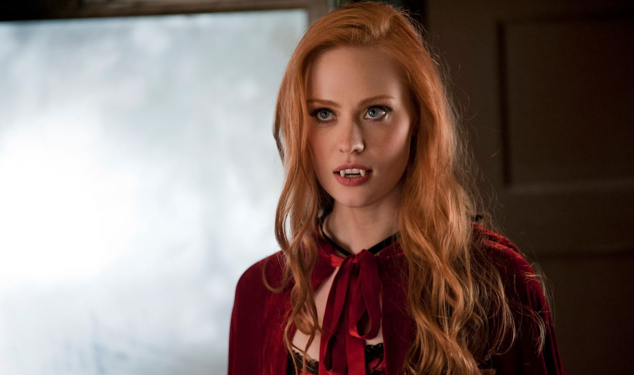 A ginger girl with bold make-up and vampire fangs wearing a red cape