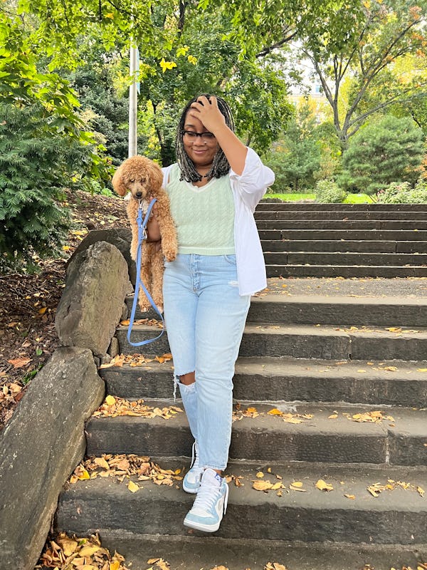 A mid-size woman walking down stairs in a green sweater vest and jeans by Abercrombie and carrying a…