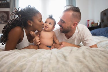 A mom and dad on a bed looking at their cute baby.